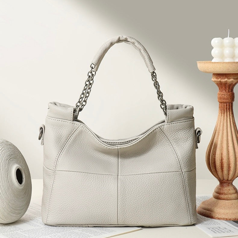 Beige handbag with chain handle on a light surface with a wooden candle holder in the background