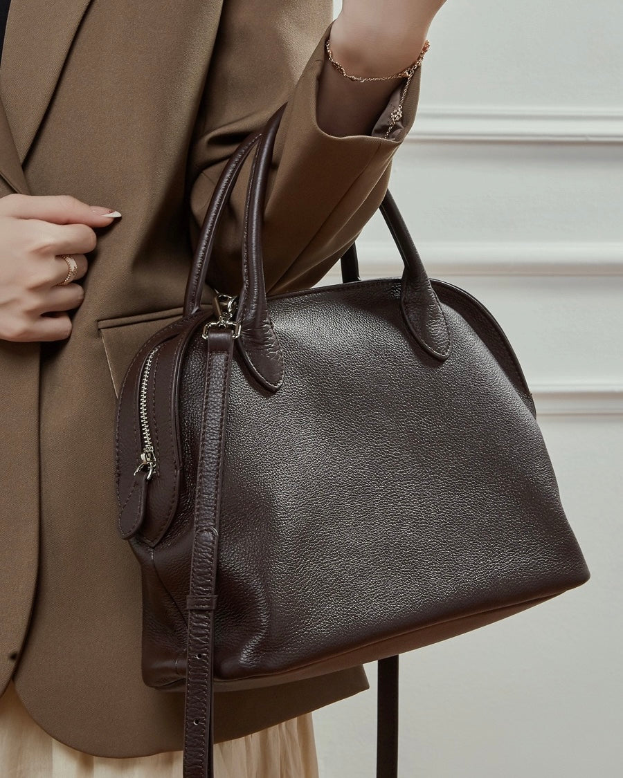 Person holding a brown handbag with a neutral background