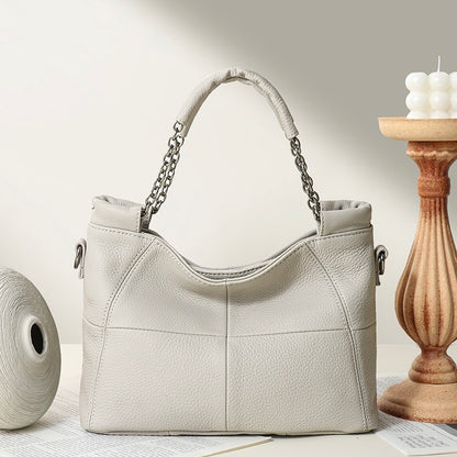 Beige handbag with chain handle on a light surface with a wooden candle holder in the background