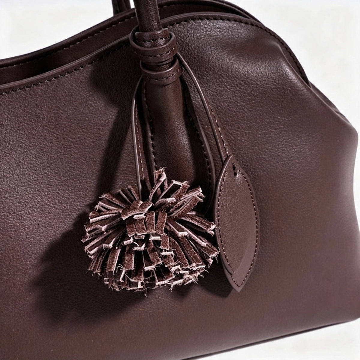 Borsa pochette minimalista curva in vera pelle morbida con ciondolo giocoso